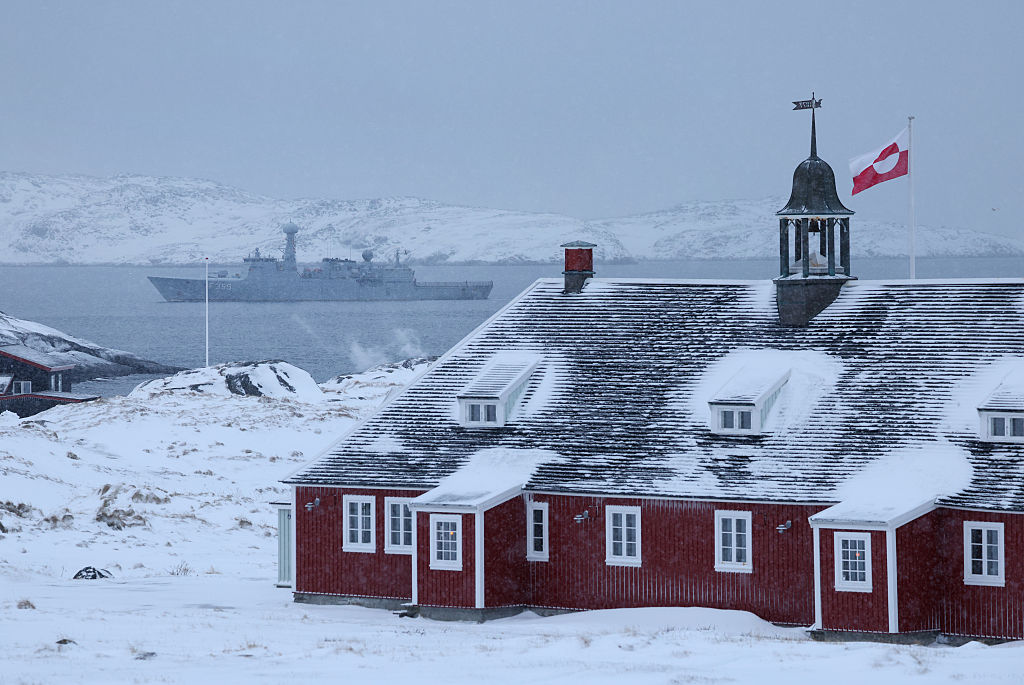 NUUK, GREENLAND - JANUARY 18: The Greenlandic flag flies over a building as the HDMS Vaedderen frigate of the Danish Navy patrols behind on January 18, 2026 in Nuuk, Greenland. Greenlandic, Danish and other European leaders are hoping they can still avert an intervention by the United States to forcefully acquire the island as U.S. President Donald Trump continues to insist the U.S. must have Greenland, suggesting even by military means if necessary. (Photo by Sean Gallup/Getty Images)
